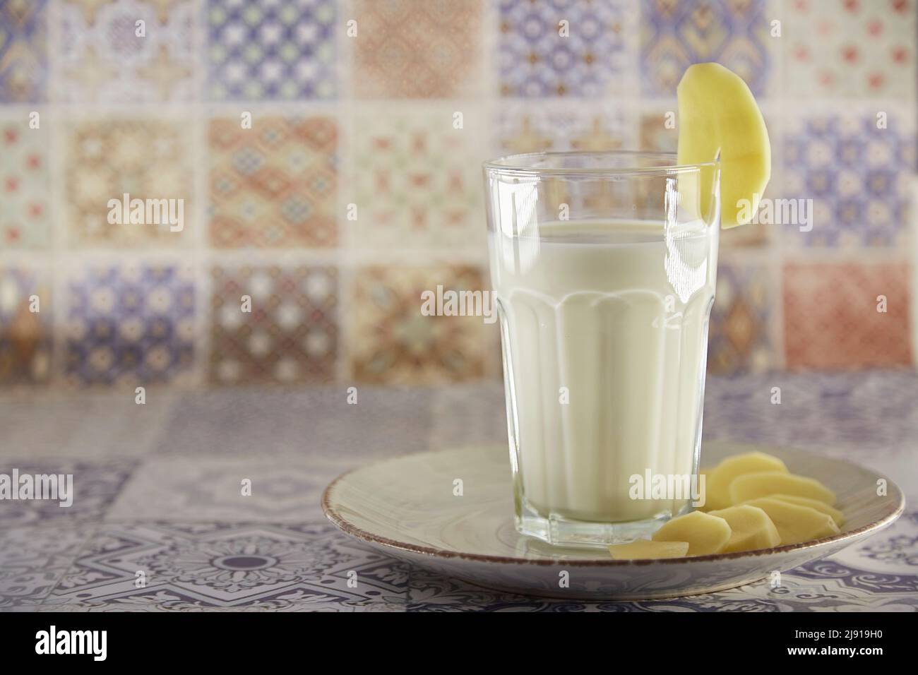 Alternative, non-dairy milk. Lactose free, environment friendly potato milk and potato on the plate on the table. Tile classic background. Copy space Stock Photo
