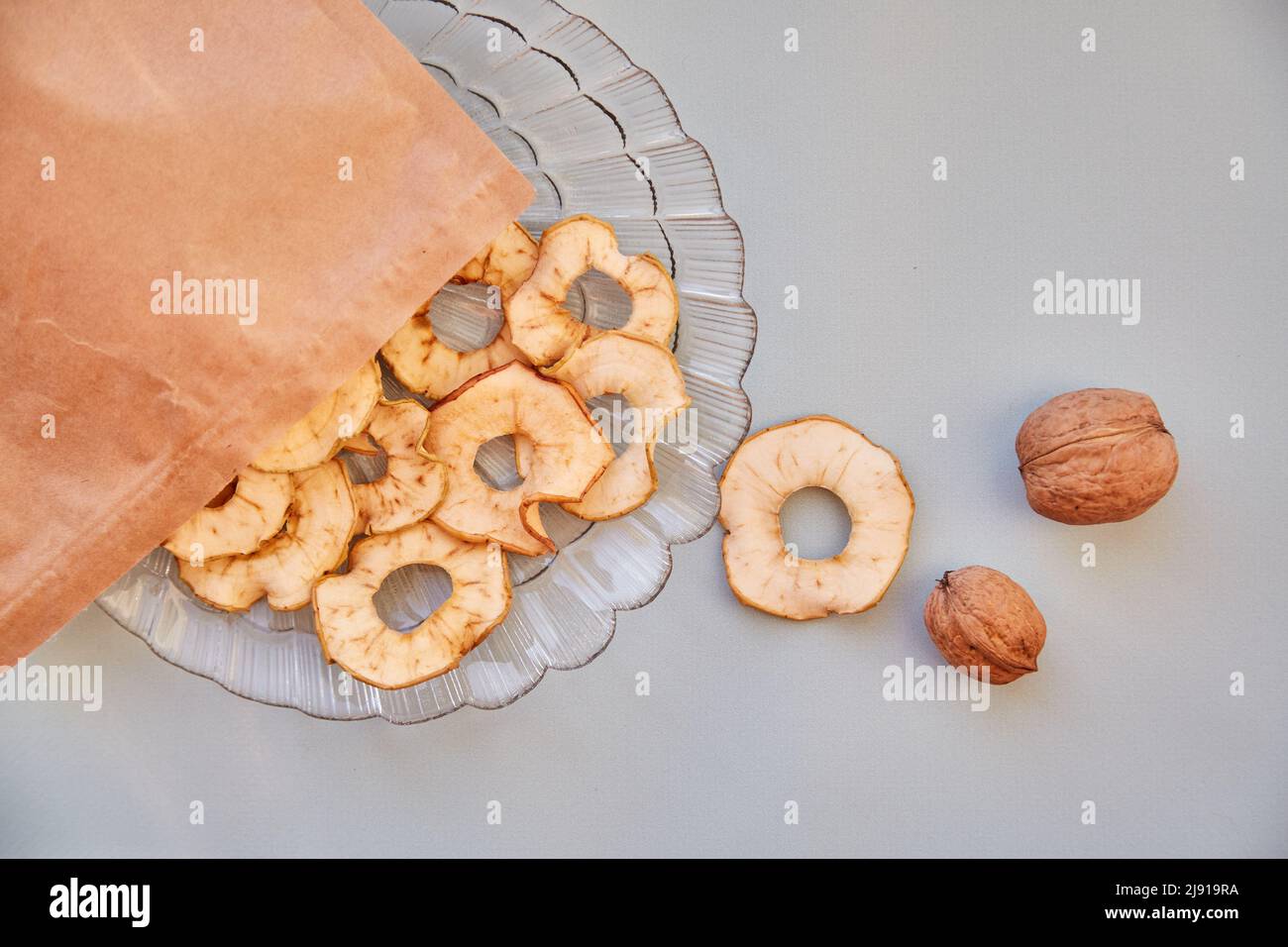 Paper bag with dried sliced apple chips and walnuts - healthy snacks on the plate. Top view. Proper nutrition, healthy food concept. High quality photo Stock Photo