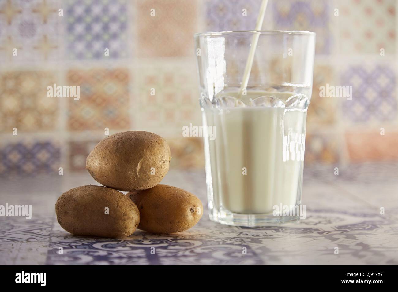 Lactose free, environment friendly potato milk and potato on the plate on the table. Alternative, non-dairy milk. Tile classic background. Copy space. High quality photo Stock Photo