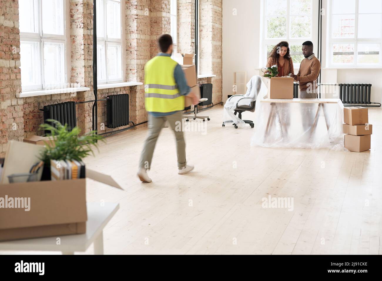 Loader carrying boxes to office owners who unpacking stuff at table ...