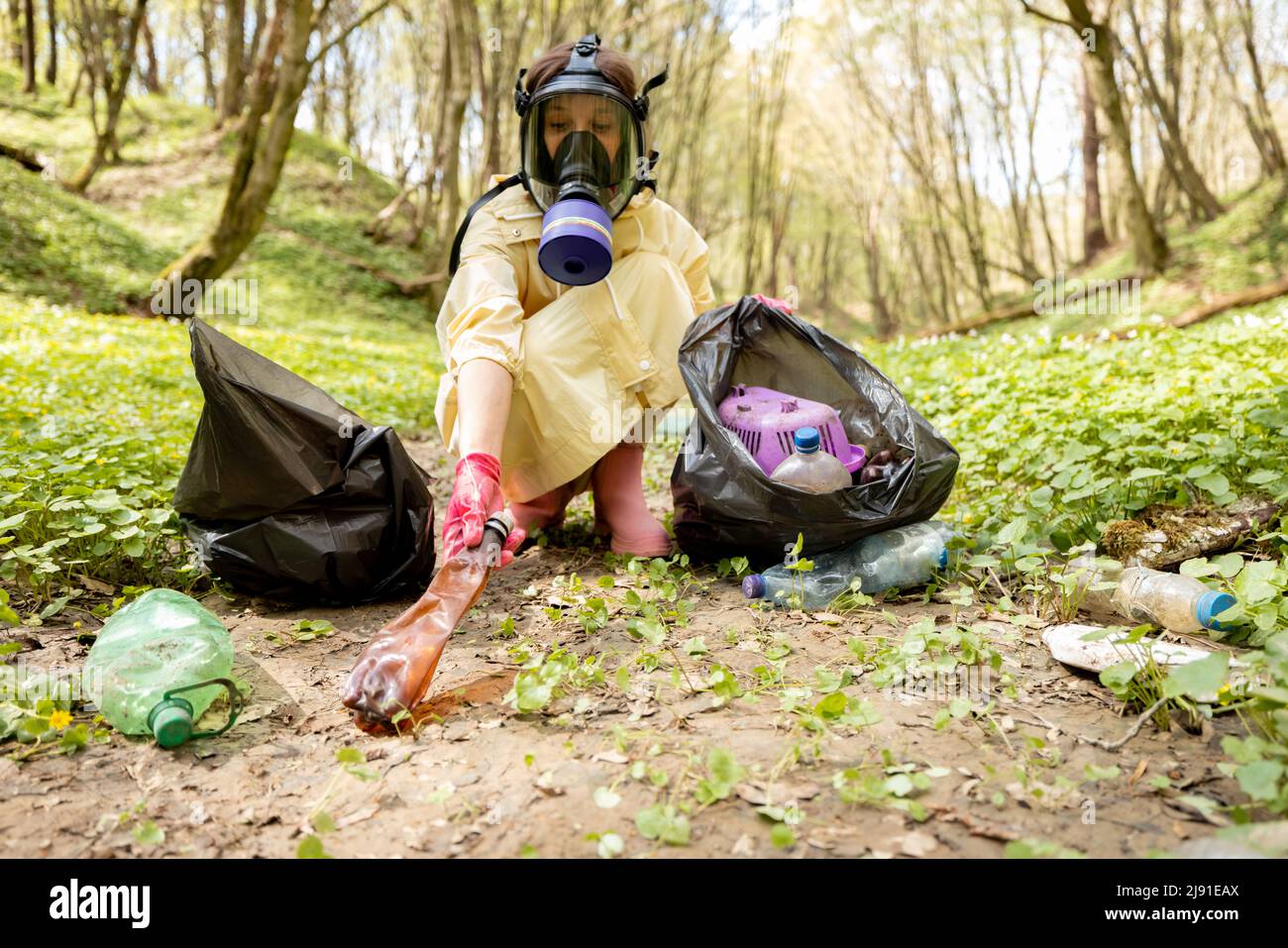 Garbege Protection Mask Woman in gas mask and protective clothes collecting scattered plastic ...