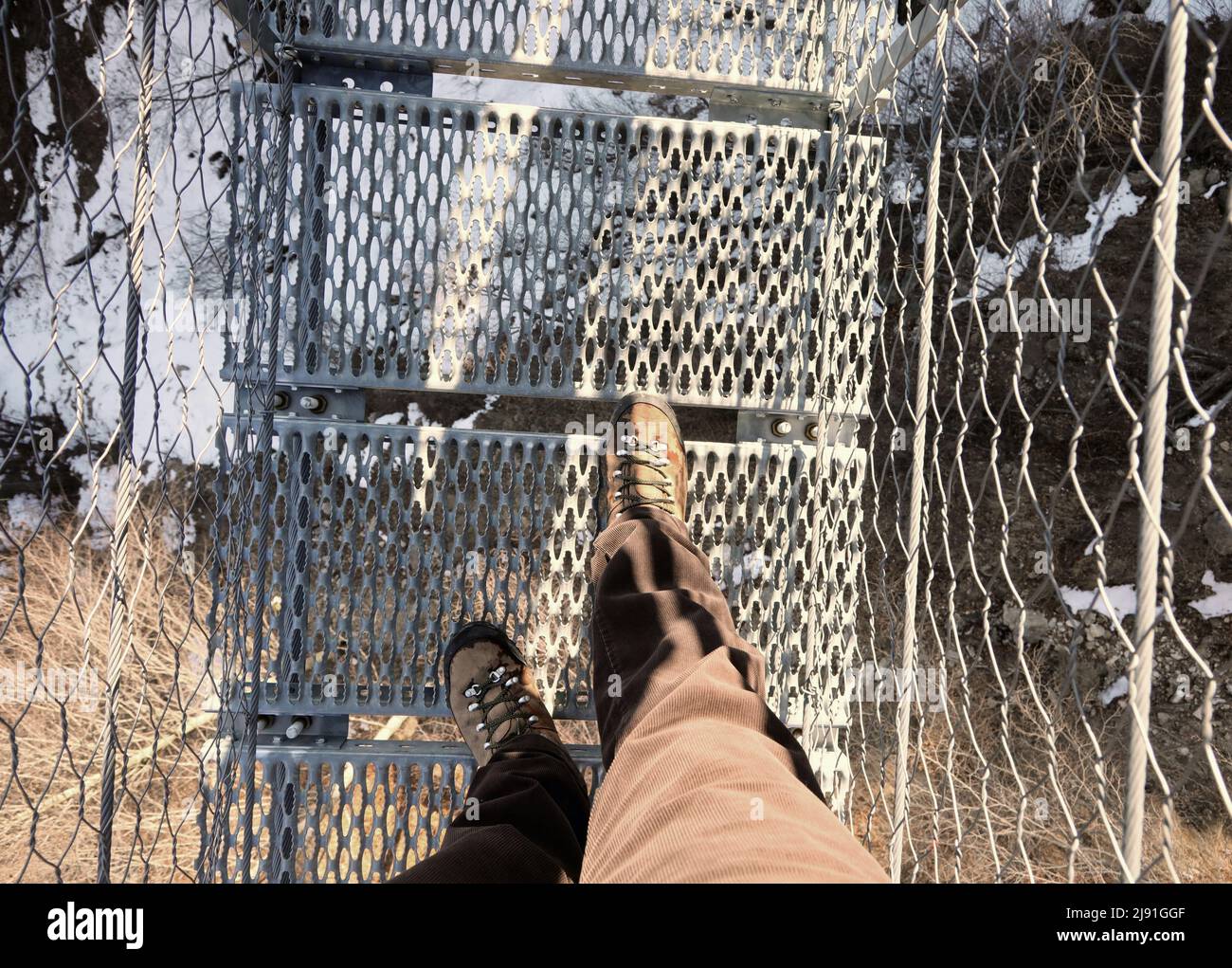 lightweight boots and legs of man on the spectacular suspension bridge made of steel ropes and metal sleepers Stock Photo