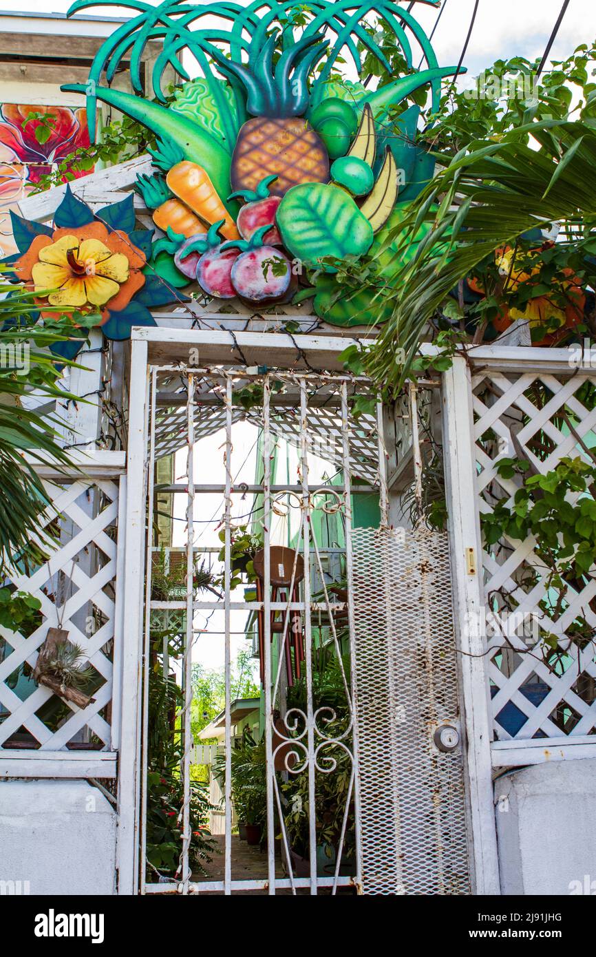 A gated entryway topped with a colorful art piece of brightly colored tropical fruits and vegetables along the street in Nassau, the Bahamas. Stock Photo