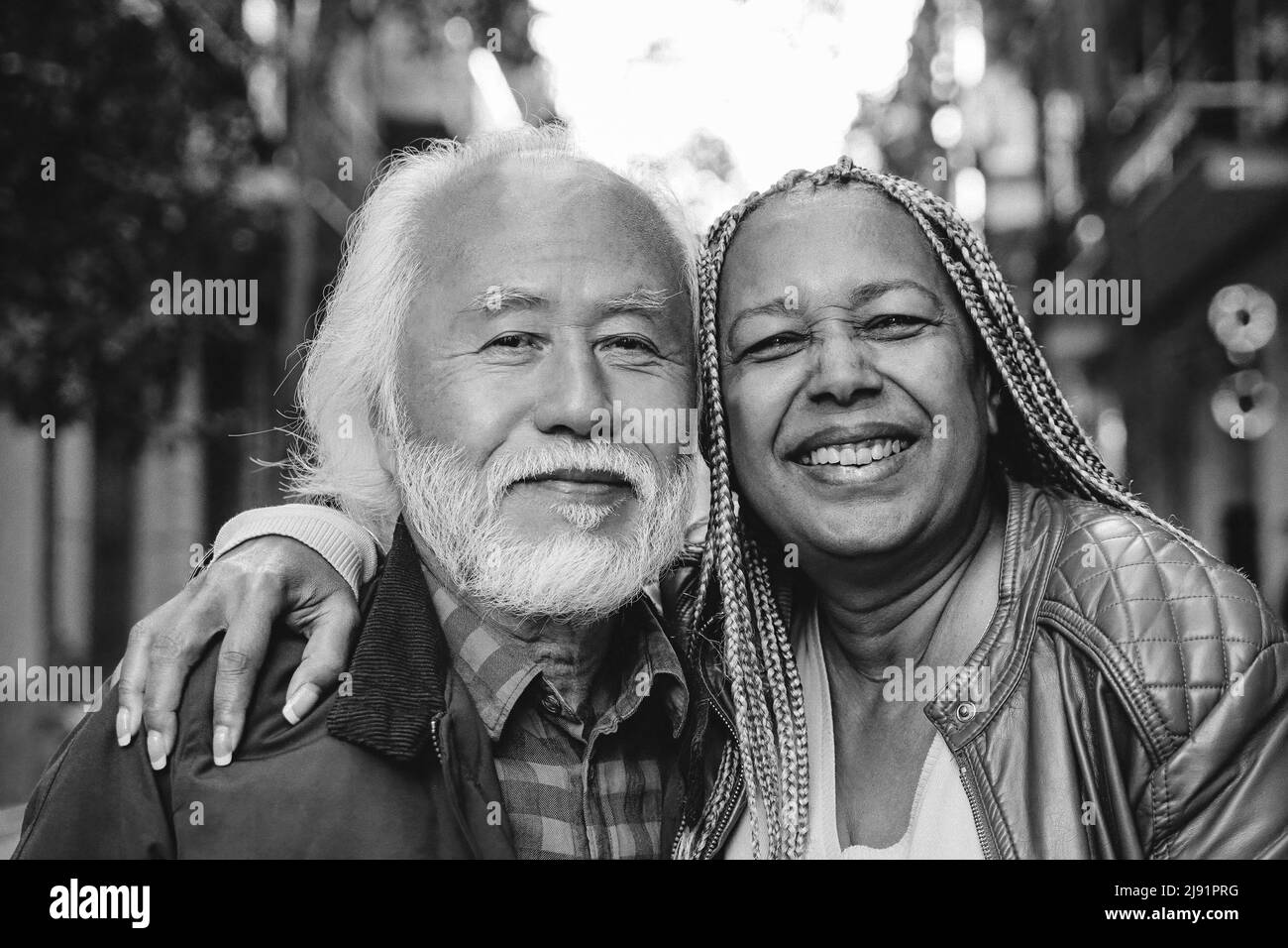 Multiethnic senior couple looking at camera outdoor - Travel, elderly people concept - Focus on african woman face - Black and white editing Stock Photo