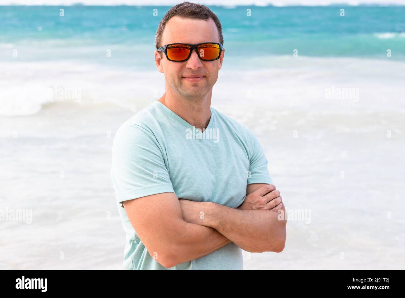 Portrait of young adult sporty man in shiny red sunglasses, outdoor photo taken on a beach on a daytime Stock Photo