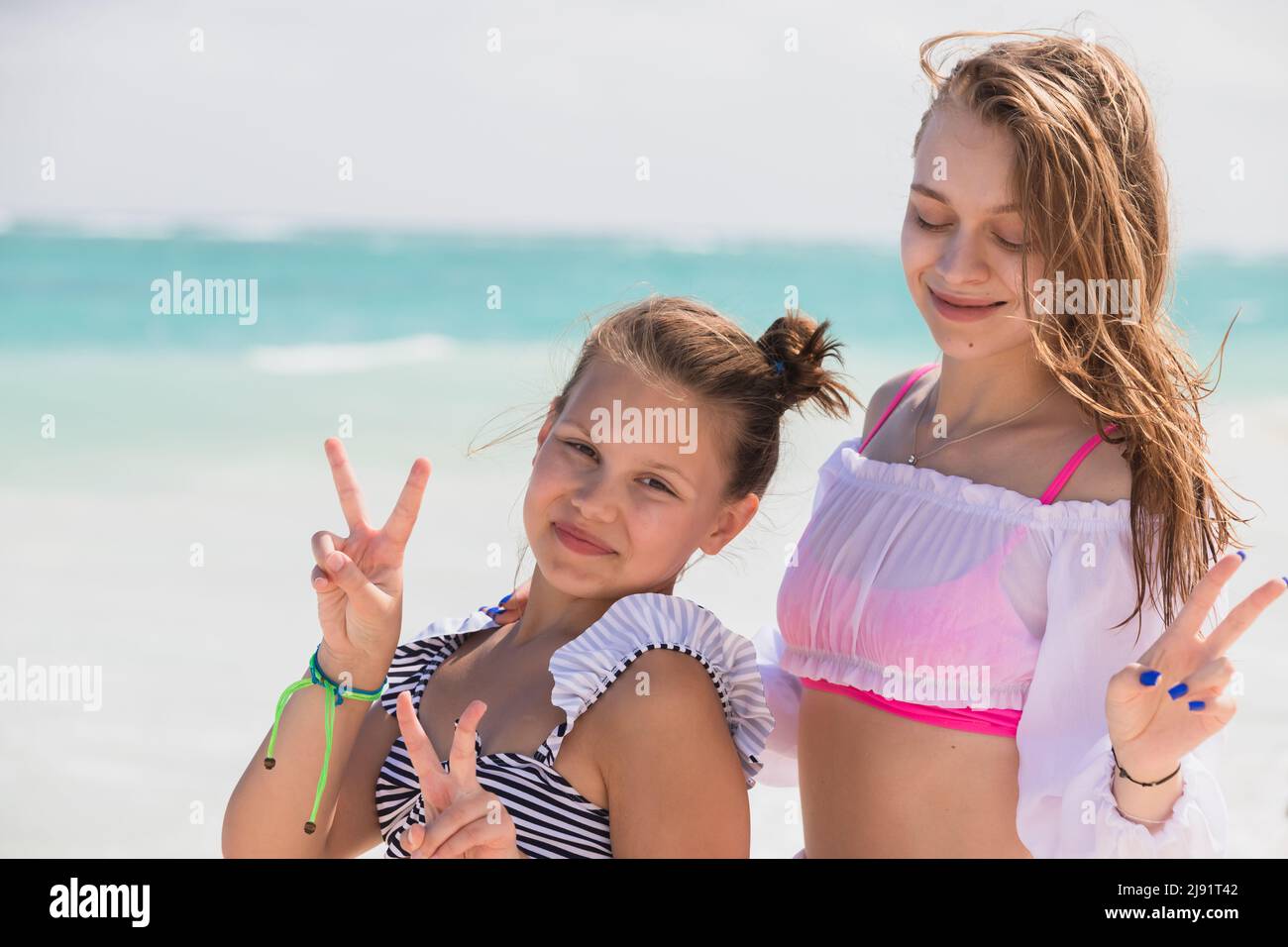 Real sisters are on the vacation. Outdoor portrait of two beautiful Caucasian girls taken at the ocean coast on a sunny day Stock Photo