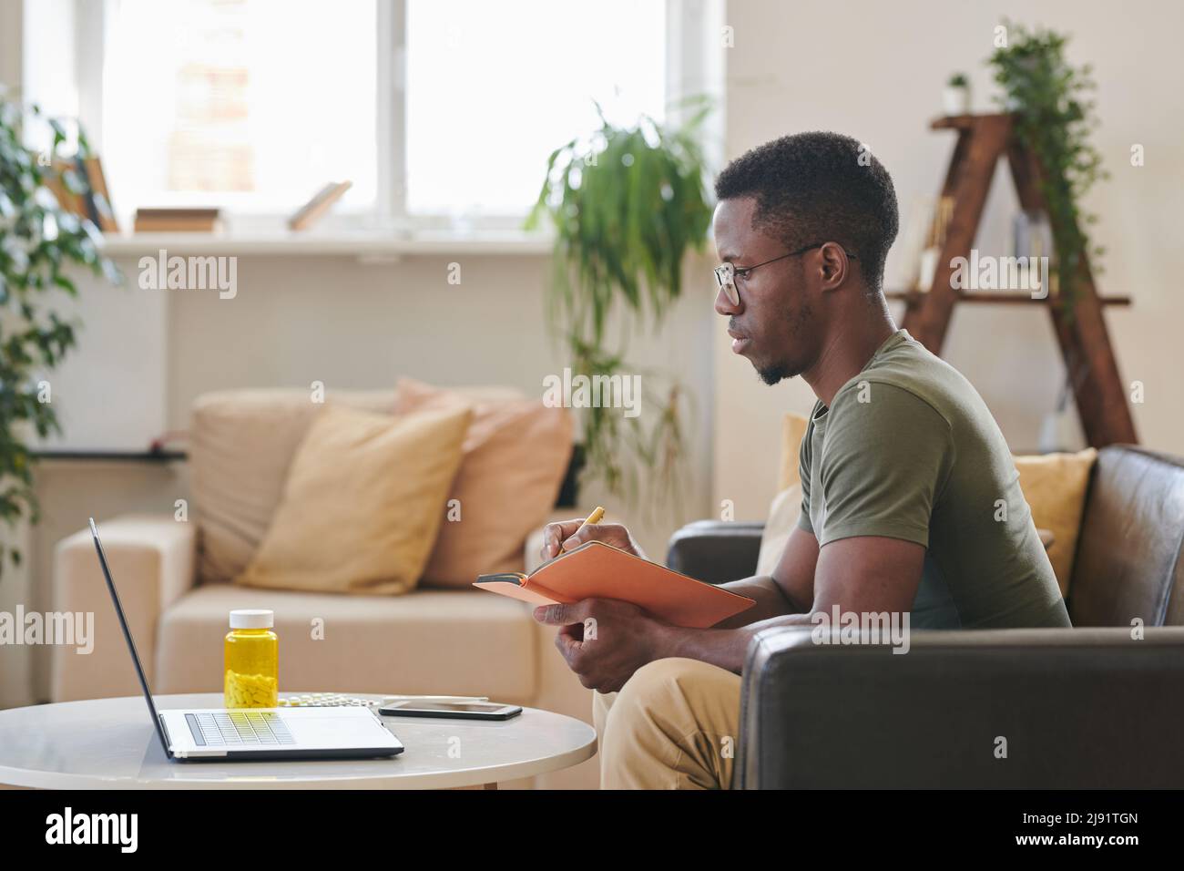 Side view shot of young adult Black man sitting on sofa in front of ...