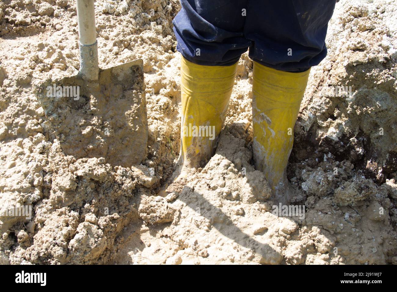 Image of the legs of a man in yellow boots sinking into the mud Stock Photo