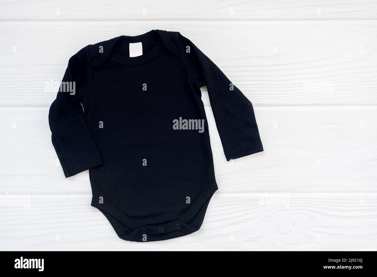 Blank black baby bodysuit long sleeve flatlay mockup on white wood background, copyspace, top view. Stock Photo