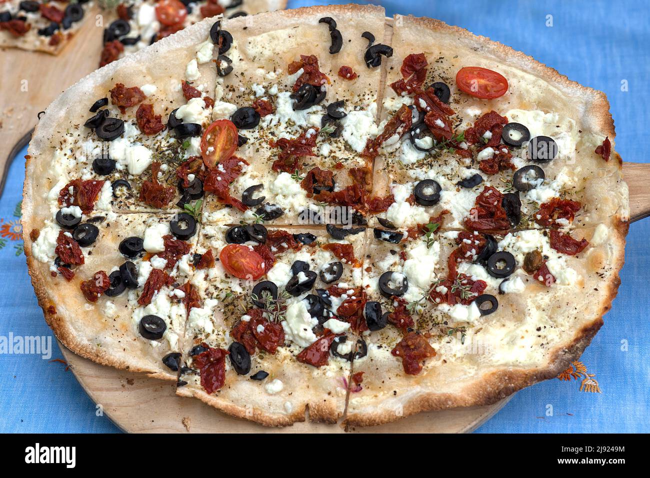 Tarte Flambee Mediterran, black olives, dried tomatoes and feta served on a wooden board, Bavaria, Germany Stock Photo