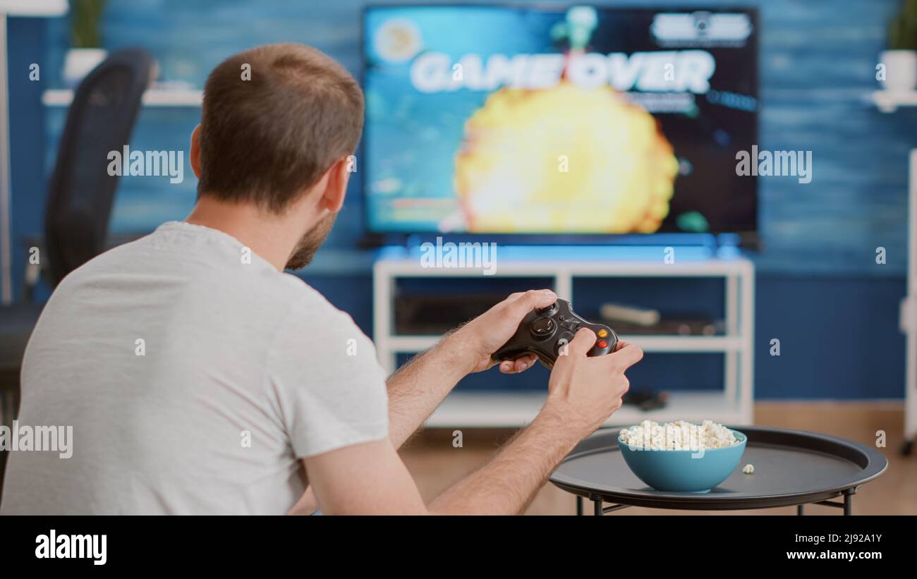 Closeup of man holding controller disappointed because losing online first person shooter game in front of big screen tv