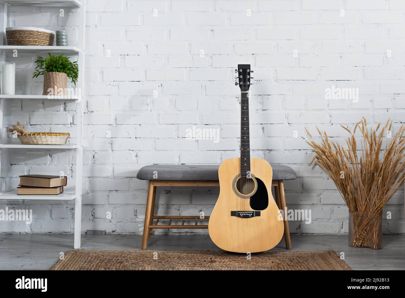 acoustic guitar, ottoman, vase with dry spikelets and rack with books