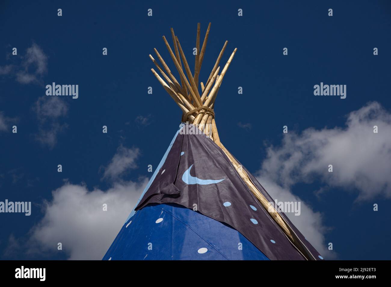 American Indian teepee poles of 24 foot structure against a blue sky with decorative canvas. Stock Photo