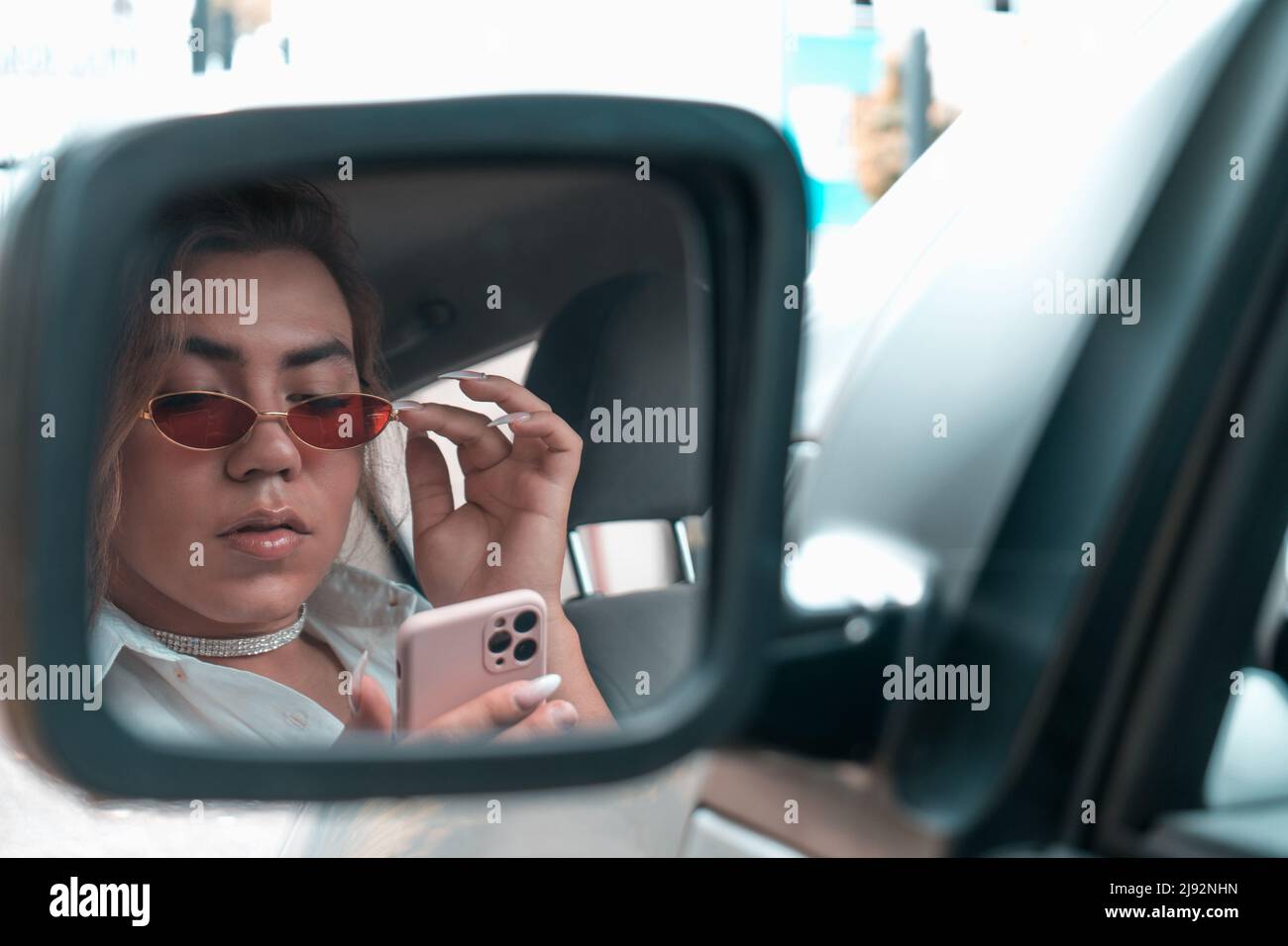 androgynous young looking your mobile at car in the rear view mirror. High quality photo Stock Photo
