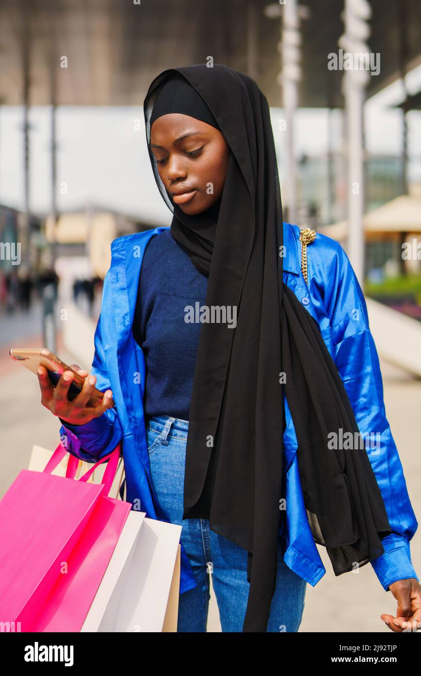 Muslim shopaholic browsing social media on street Stock Photo