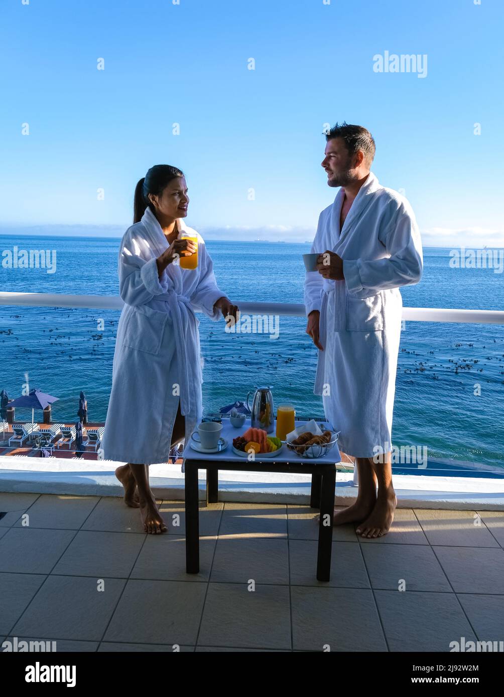 Cape Town South Africa couple man and women drinking coffee during on balcony sunrise at vacation in Cape Town South Africa. European men and Asian women waking up with coffee looking out over the ocean Stock Photo