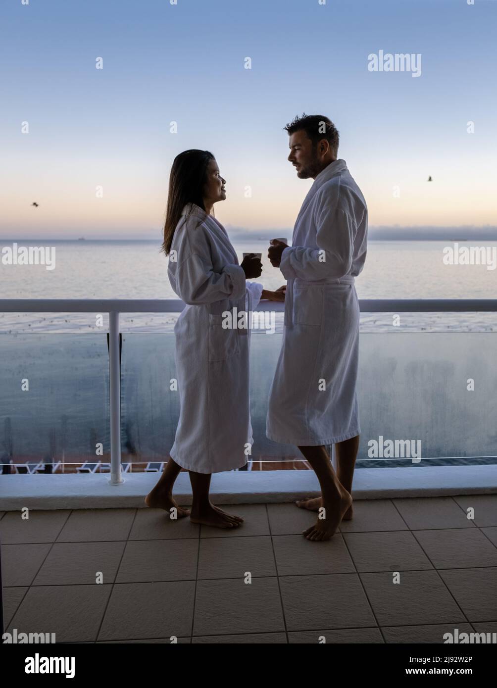 Cape Town South Africa couple man and women drinking coffee during on balcony sunrise at vacation in Cape Town South Africa. European men and Asian women waking up with coffee looking out over the ocean Stock Photo