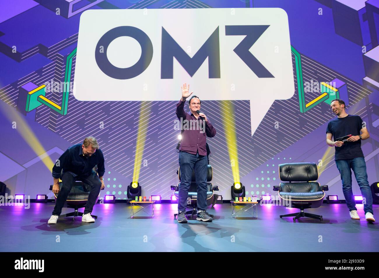 Hamburg, Germany. 18th May, 2022. Director Quentin Tarantino (M) stands waving on stage between presenter Steven Gätjen (L) and OMR CEO Philipp Westermeyer (R). The OMR digital festival in Hamburg is a combination of trade fair, workshops and party. Credit: Jonas Walzberg/dpa/Alamy Live News Stock Photo
