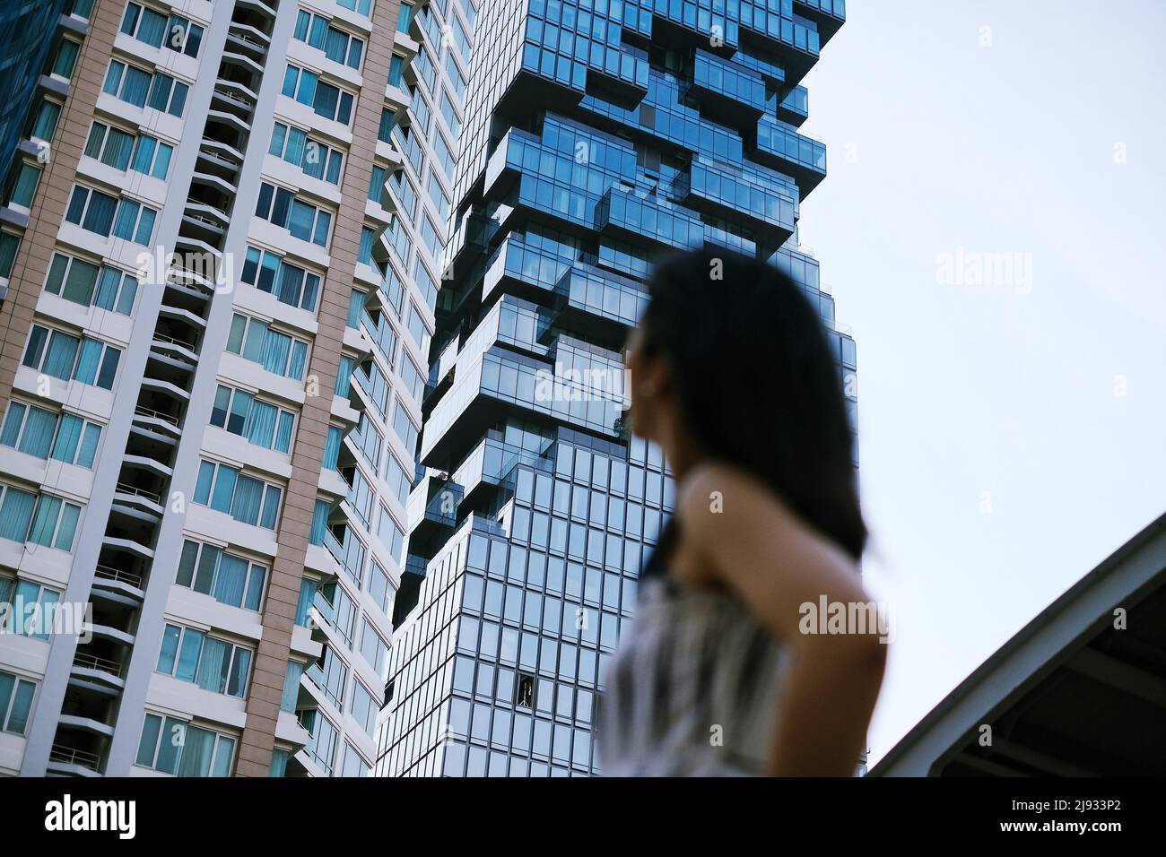 The view of high rise buildings in central Bangkok, Thailand with an out of focus woman looking up at the skyscraper in the foreground. Stock Photo