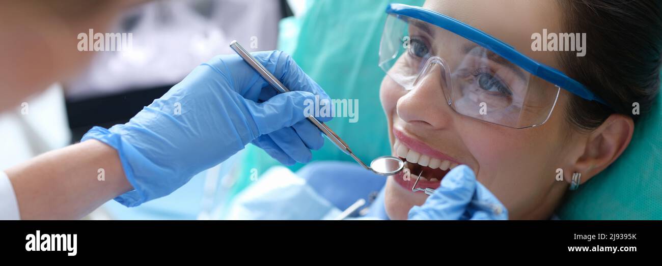 Doctor examining oral cavity of female patient using dental instruments in clinic Stock Photo