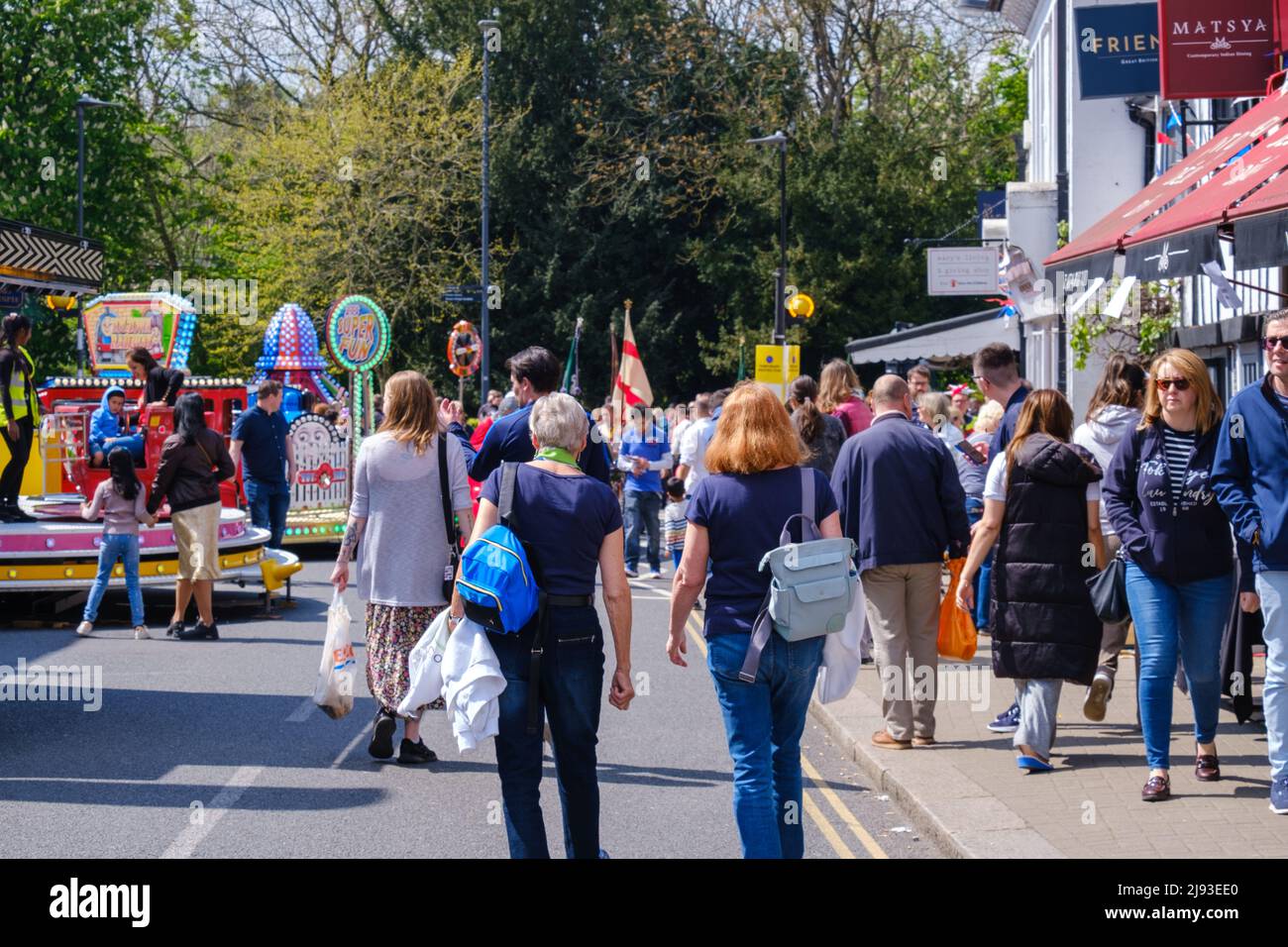 Children’s rides & people walking in street & pavement at 2022 St George’s Day Celebration. Pinner, Harrow, Greater London, England. Stock Photo