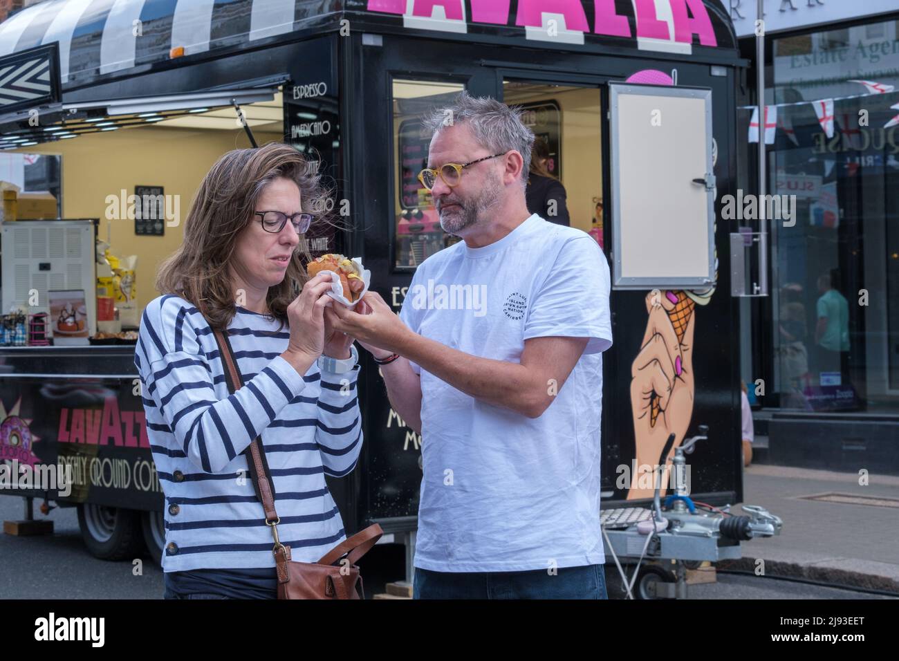 Man with glasses helps a woman with her street food hotdog at 2022 St George’s Day Celebration at Pinner, Harrow, Greater London, England. Stock Photo