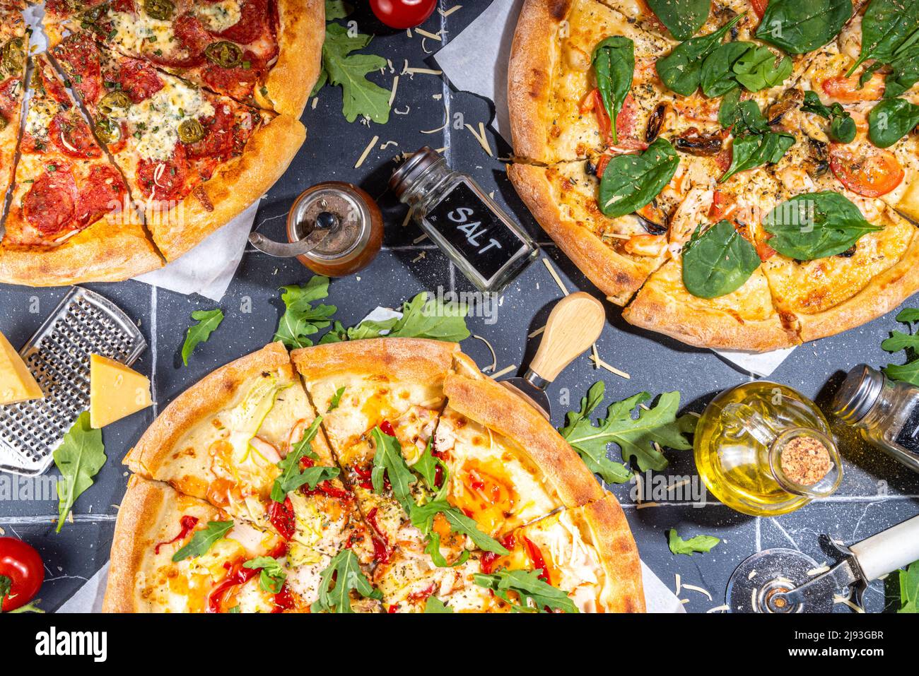 Three various pizzas, served at home or in restaurant on tiled table with cooking ingredients