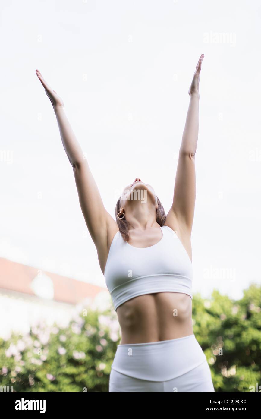 low angle view of woman in white sports bra training with raised hands outdoors Stock Photo