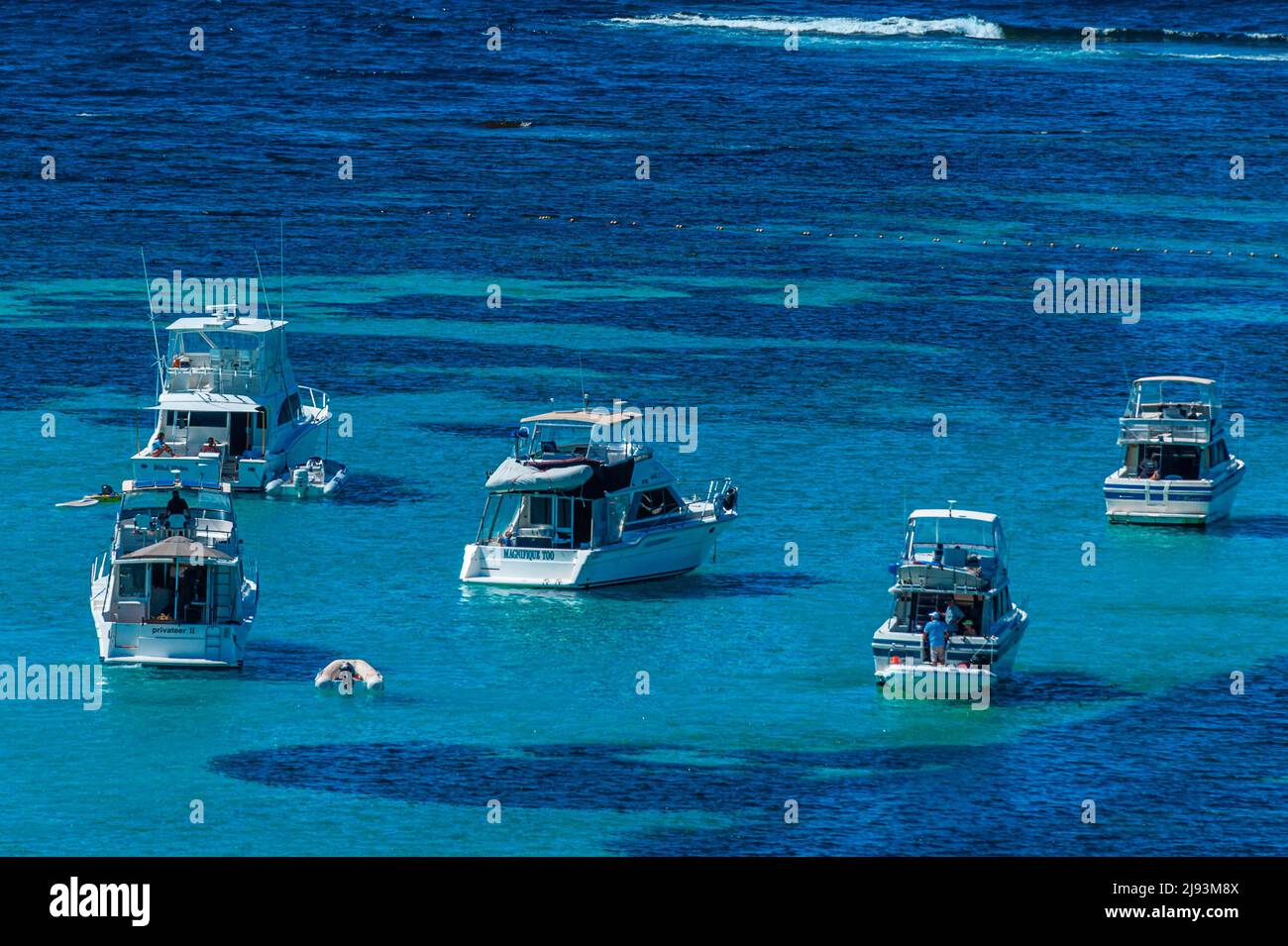 Five fishing and pleasure cruisers anchored over a reef, with fishing rods visible. Stock Photo