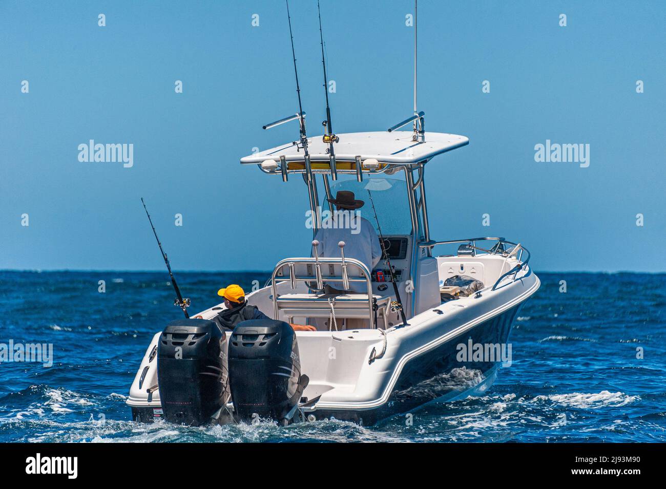 Twin outboard motors power a fishing and pleasure cruiser at sea, with fishing rods visible. Stock Photo