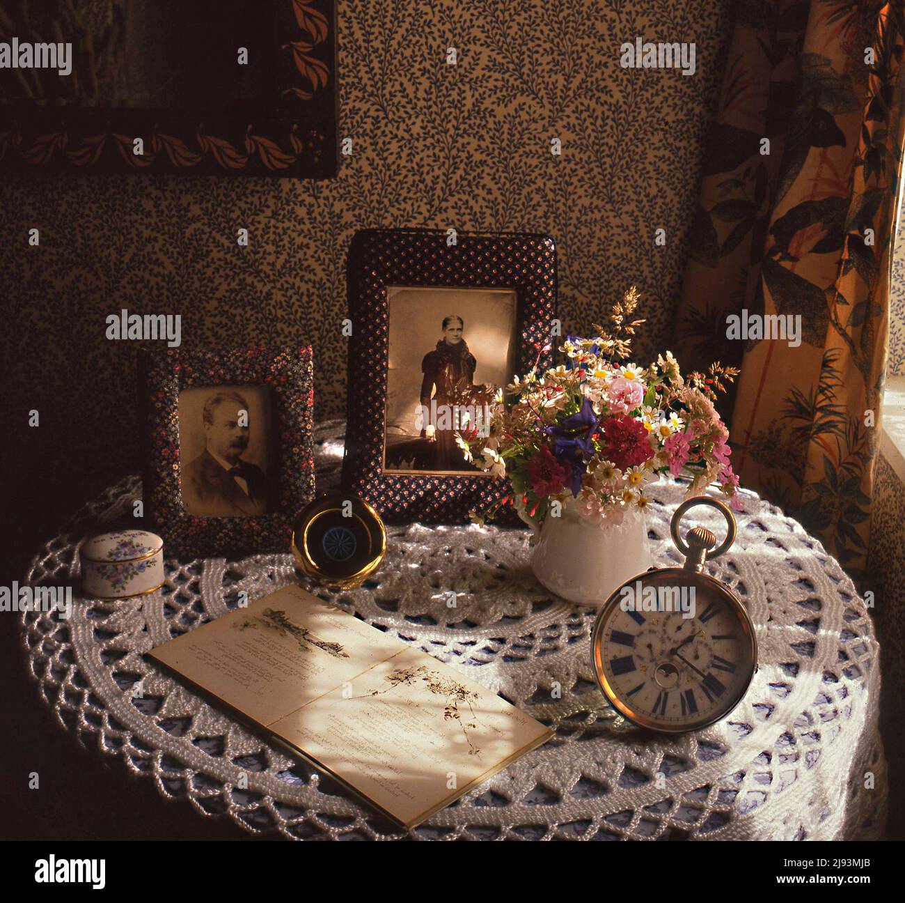 Period still life table setting with picture frames and an old clock, illuminated by window lighting. Stock Photo