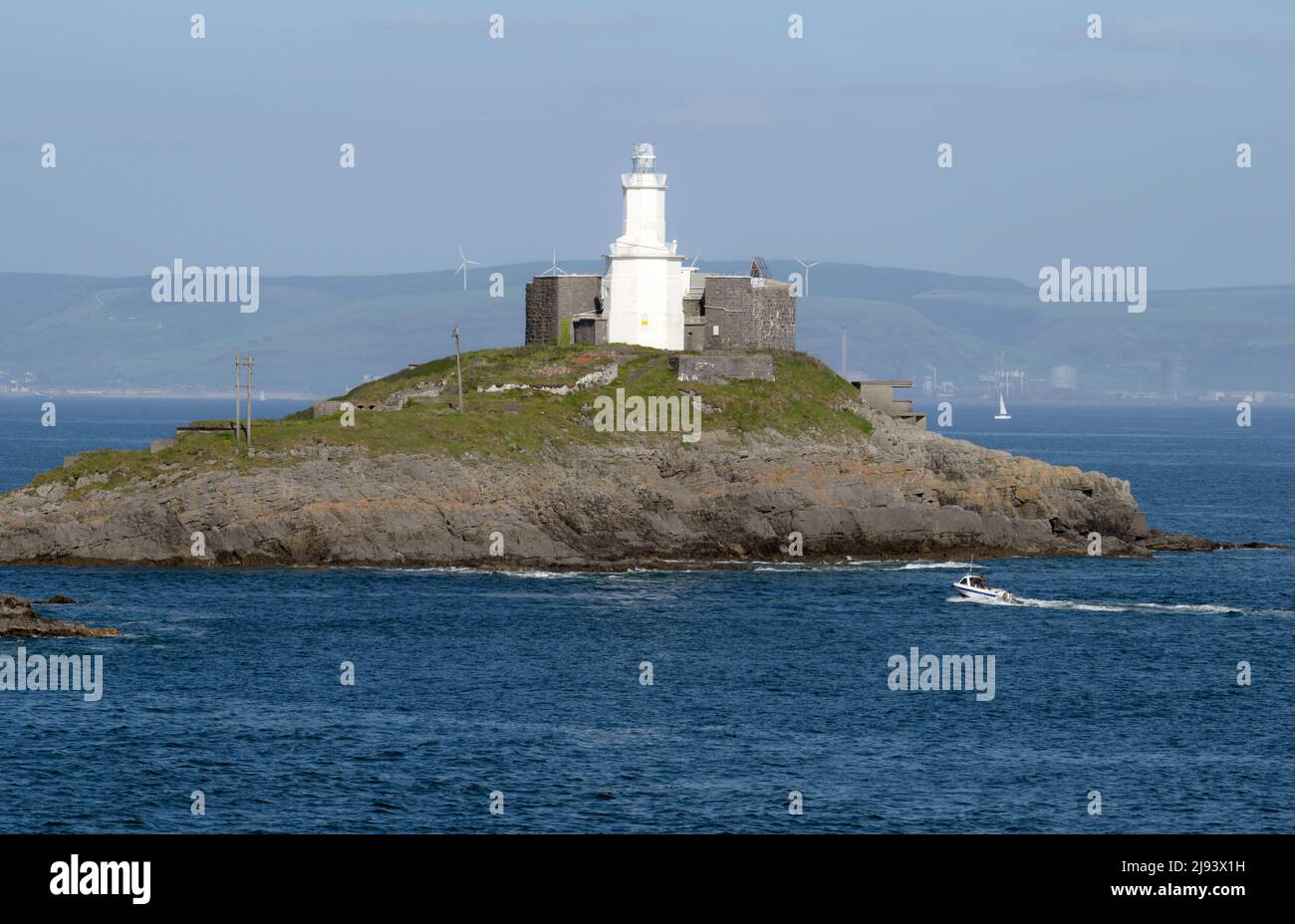 Mumbles lighthouse perched on its own island at high tide A fishing boat is passing through the outer causeway of the headland into swansea bay Stock Photo