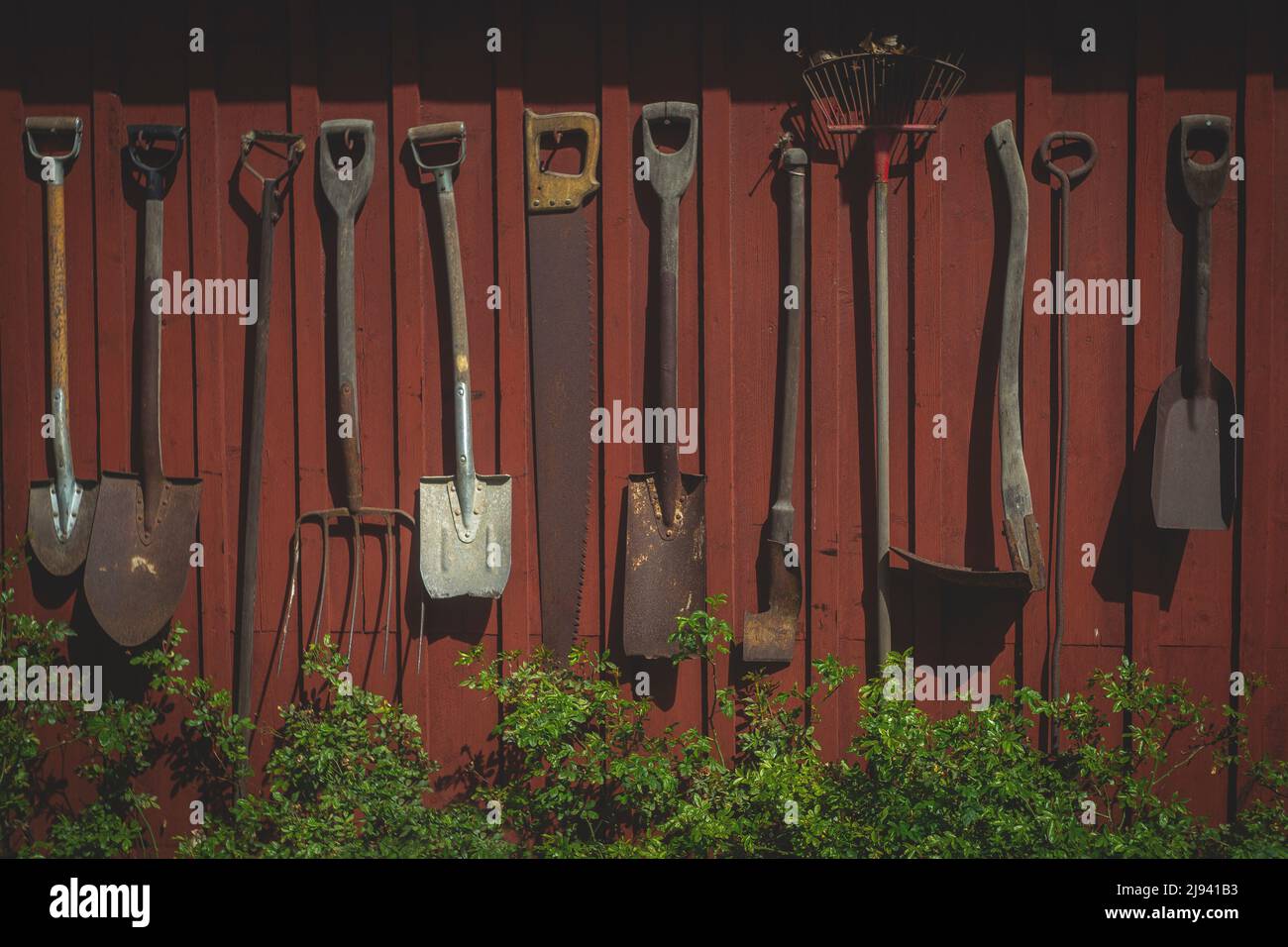Antique gardening tools in the tourist town of Sigtuna hang on the wall of a red wooden house Stock Photo
