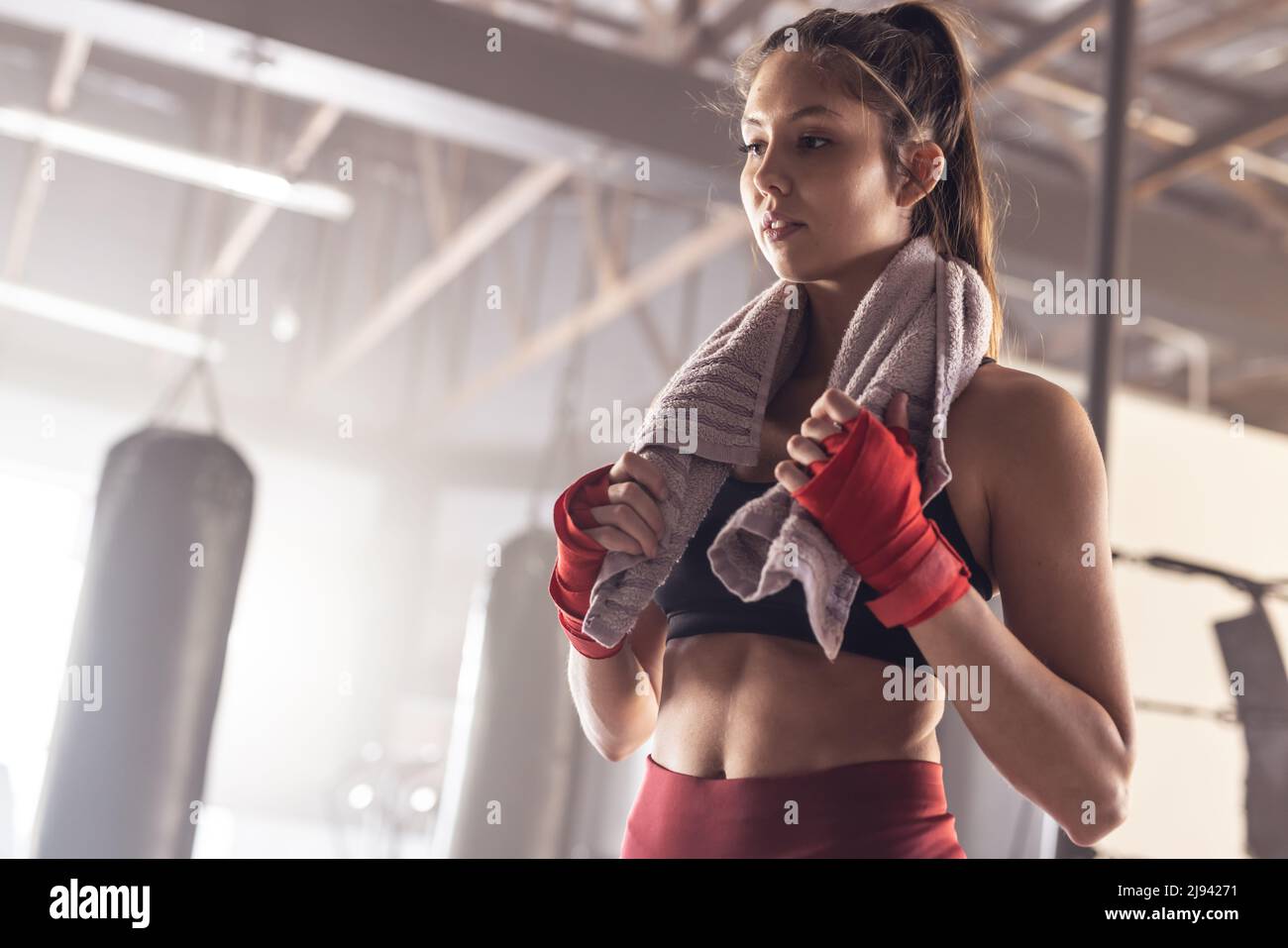 Low angle view of thoughtful caucasian young female boxer with towel around neck in health club Stock Photo