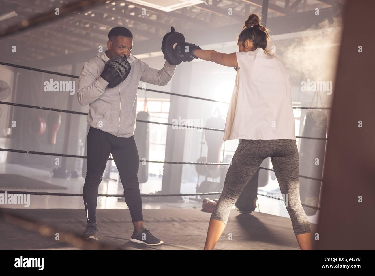 African american young male coach wearing boxing paws giving training to caucasian female boxer