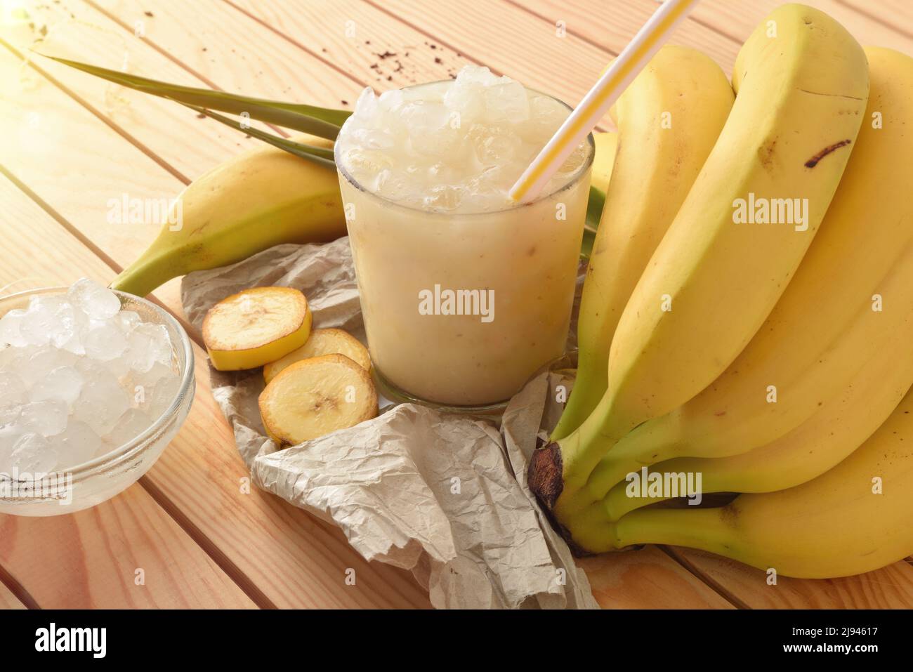 Glass of cold banana drink with ice on wooden table with fruit. Elevated view. Horizontal composition. Stock Photo