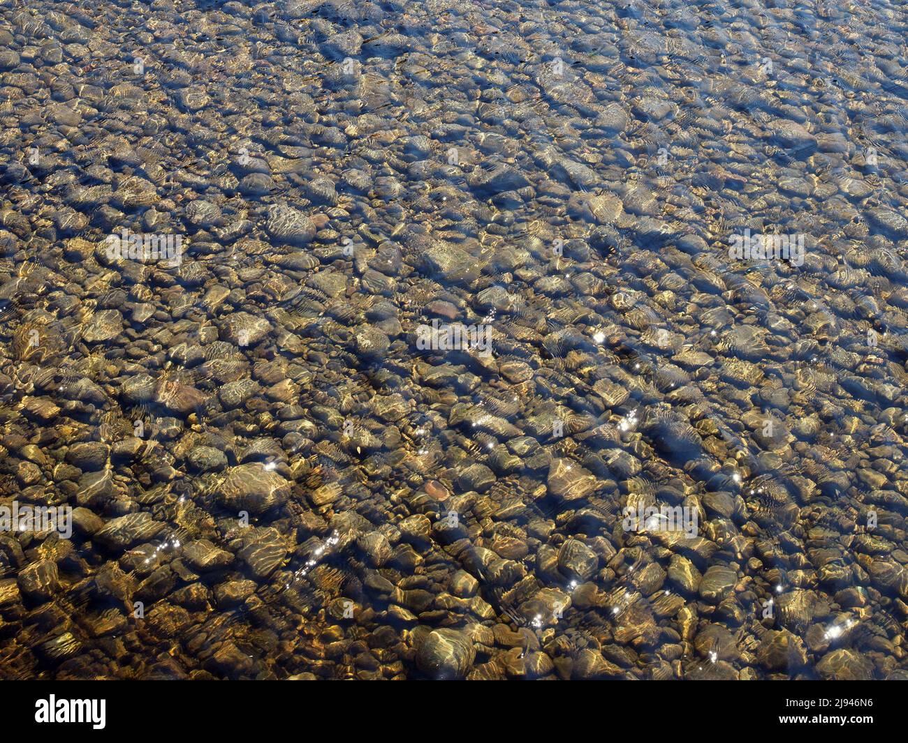 Clear shallow water flowing over river bed of smooth pebbles on a bright sunny day. Stock Photo