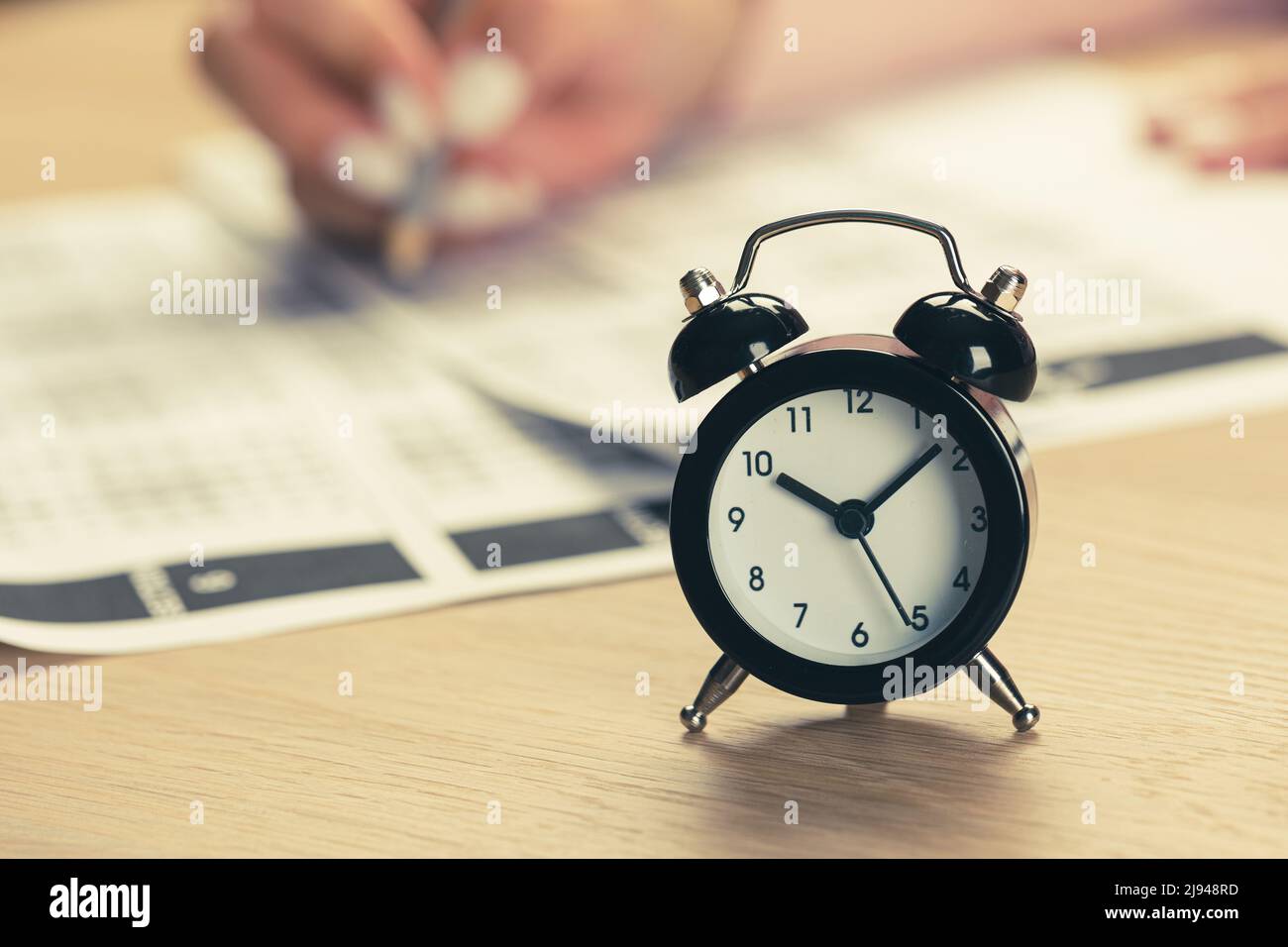 alarm clock with time running out. Students hands to take exams, write examination room with