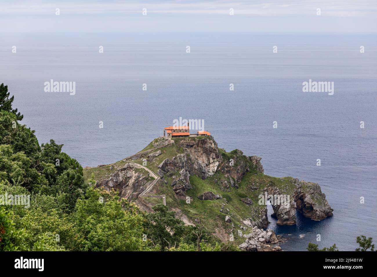 Cantabrian Sea ceaselessly erodes rocky coast creating tunnels, arches, and caves on Gaztelugatxe island with 9th-century church on 80 meters Stock Photo