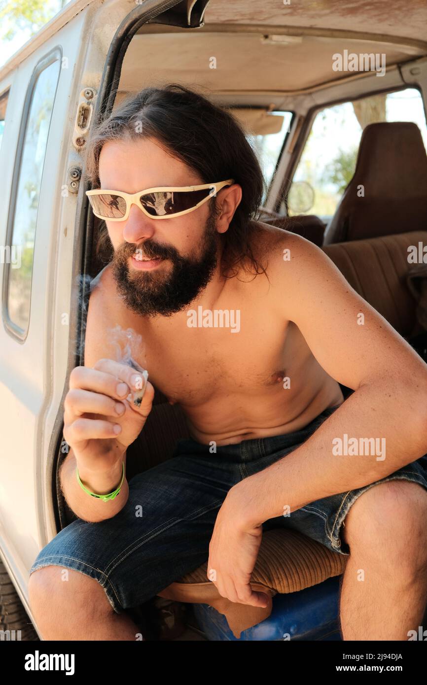 Happy smiling man smoking cbd weed in a van at cannabis festival. Summer sea trip. Marijuana joint. Stock Photo