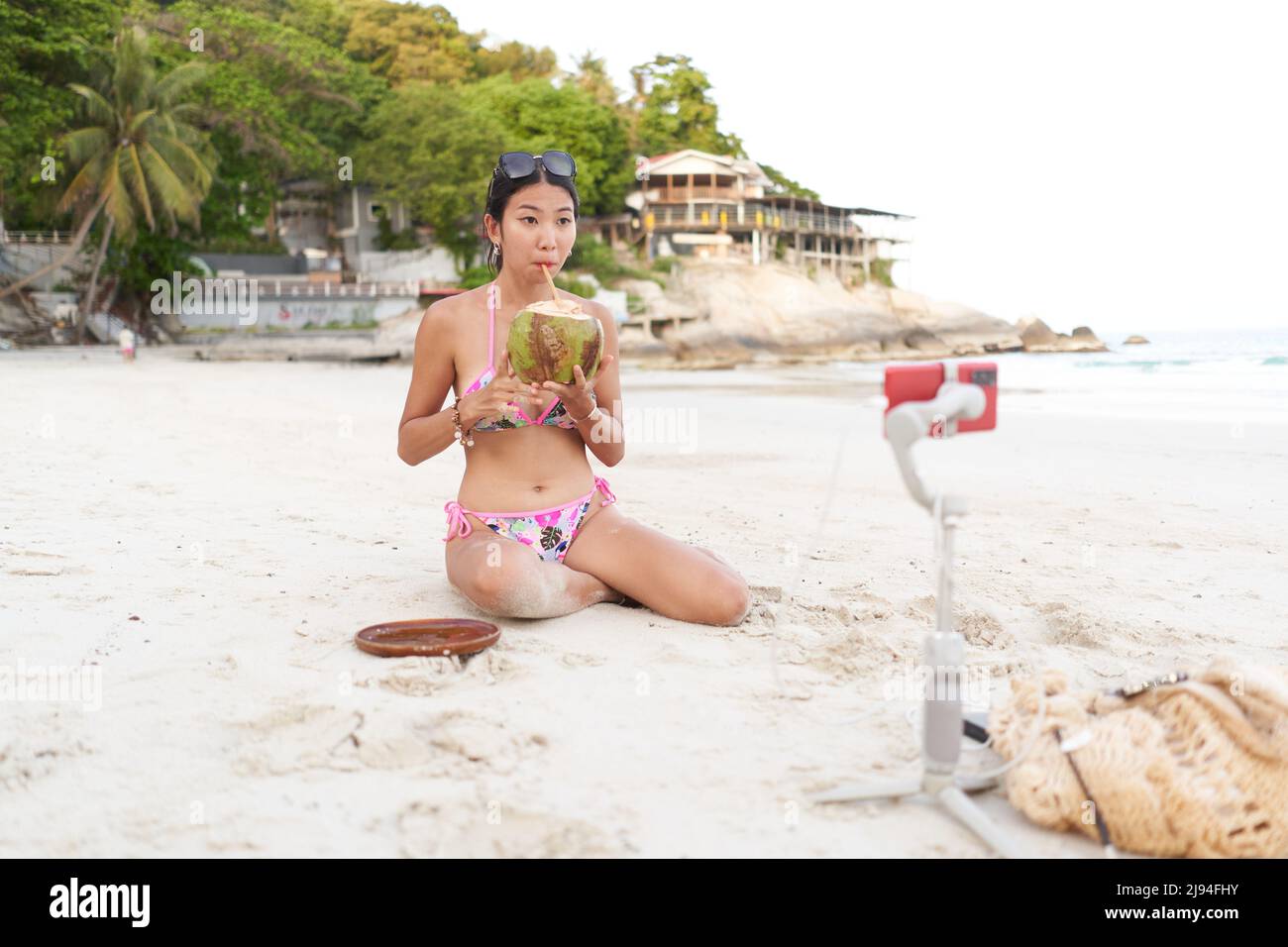 Streamer drinking a coconut juice while doing a live using a mobile on the beach Stock Photo