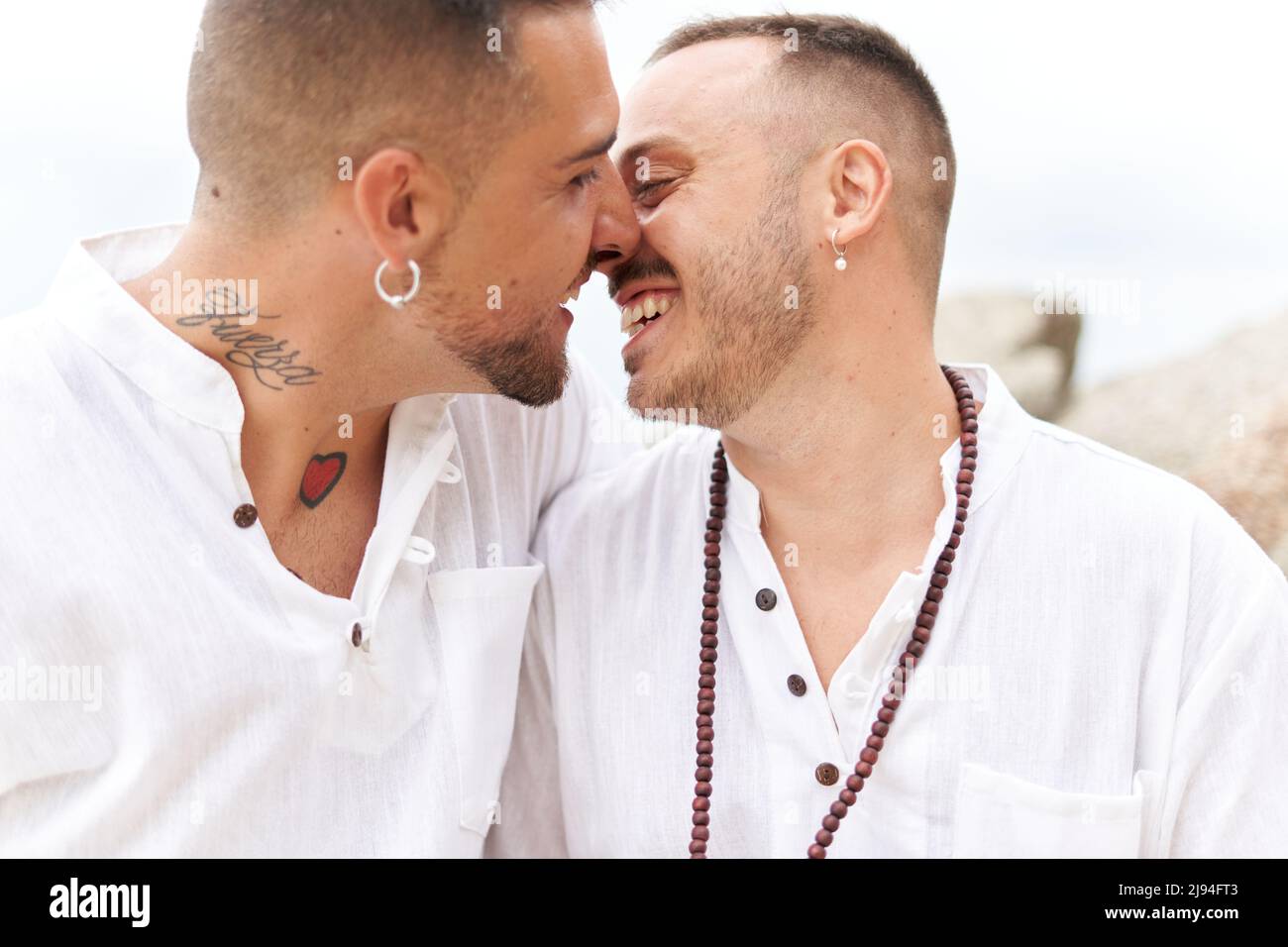 Close up photo of a gay couple smiling tenderly while kissing next to the sea Stock Photo
