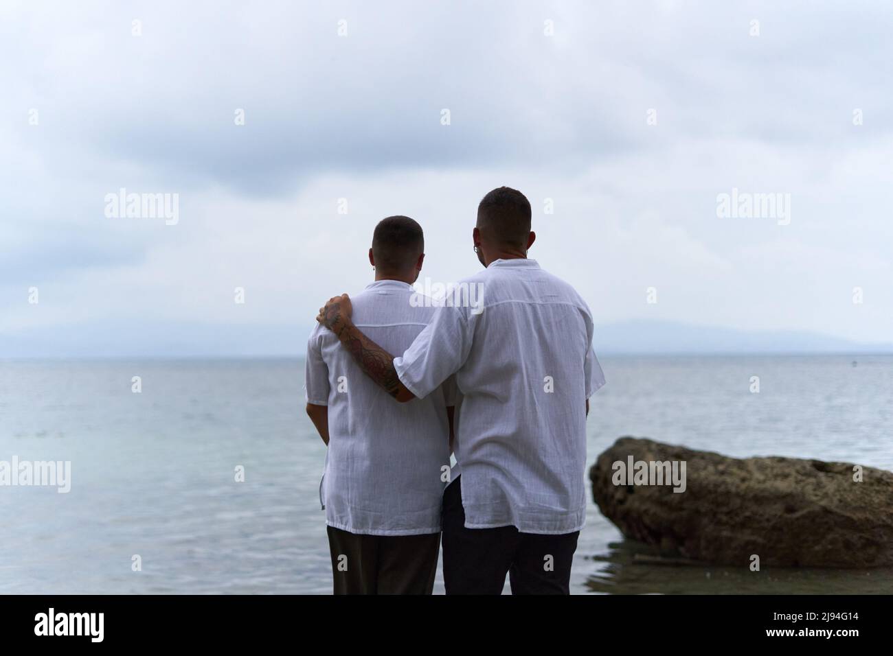 Gay couple gazing at the horizon of the ocean as they embrace in the evening Stock Photo