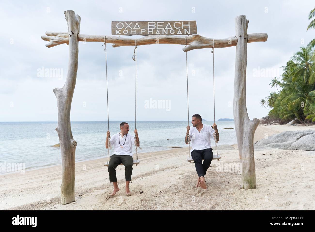Homosexual couple swinging on a swing in a tropical beach Stock Photo
