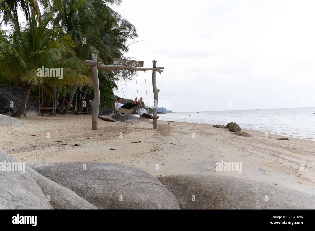 Homosexual couple swinging on a swing in the middle of a beach Stock
