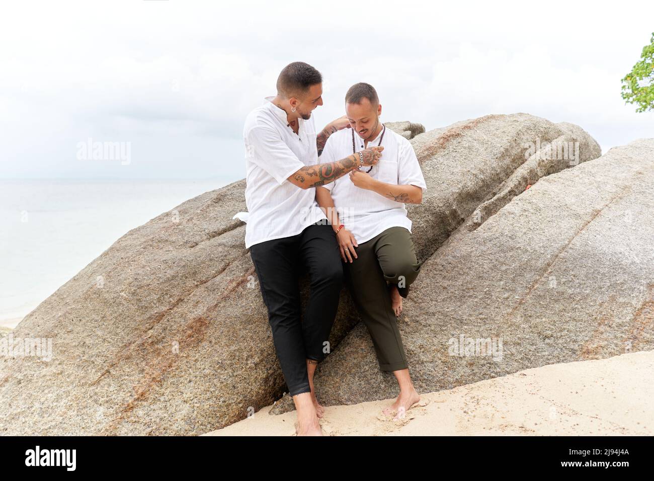 Homosexual man putting on a ball necklace to his partner in a tropical beach Stock Photo