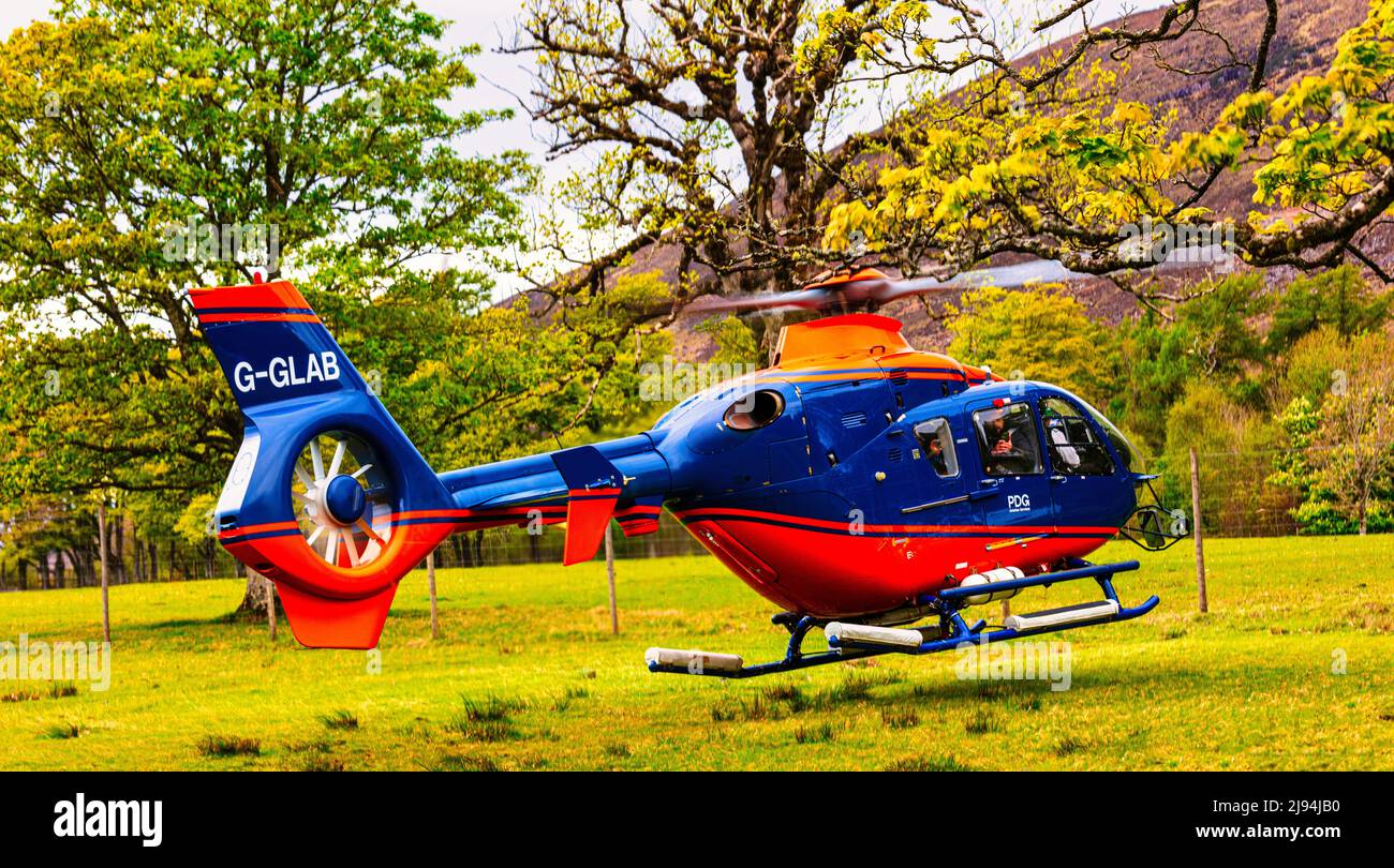 Blue and red G-GLAB - Airbus Helicopter H135 hovers in preparation   for take off, Applecross Peninsula  ,Bealach na Ba,  North Coast 500, Scotland Stock Photo