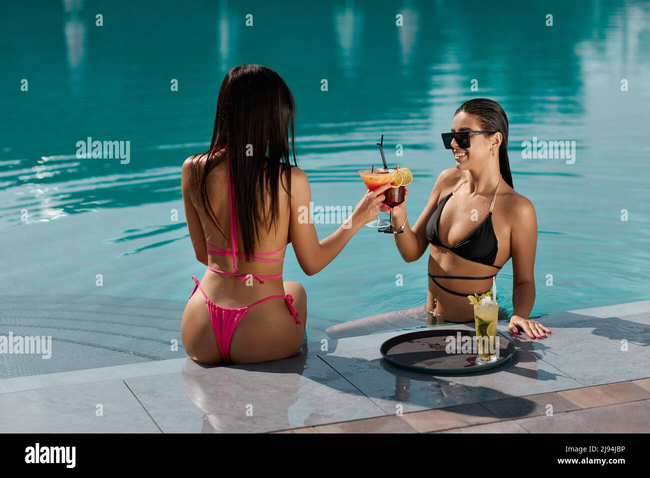 Two happy woman in bikini holding glasses of fresh cocktail to