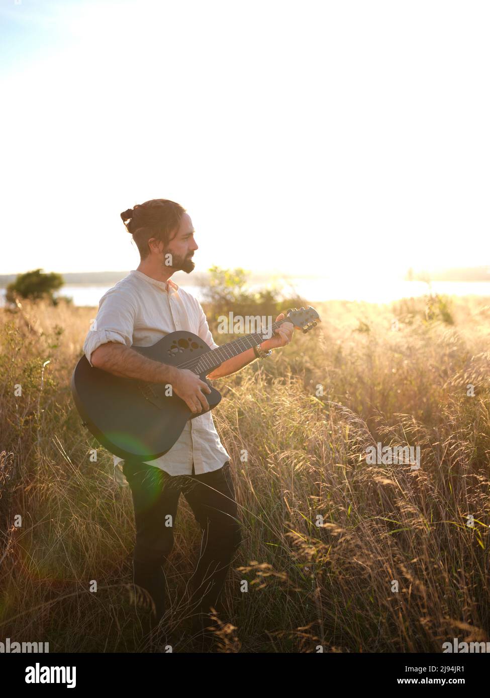 man standing with a guitar with the sunset on the horizon Stock Photo