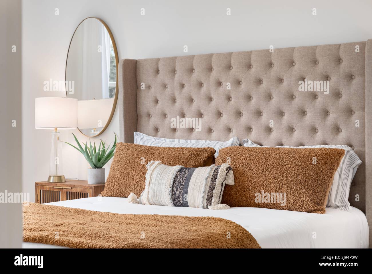 A bedroom detail shot with a cushioned headboard, a gold mirror on the